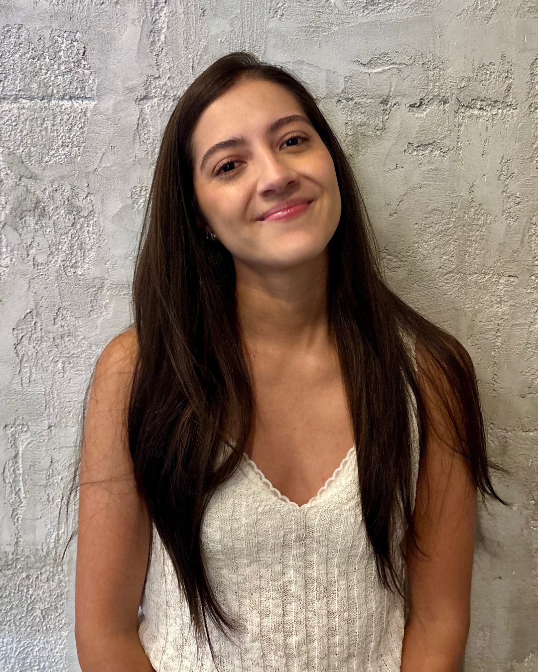 Andrea González, sonriente, sobre un fondo de pared texturizada en tonos neutros